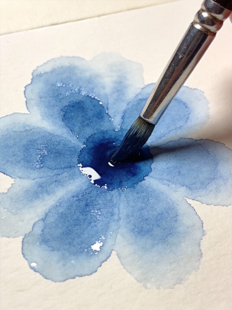 Blue watercolor paint spreading on wet paper from brush contact showing wet-on-wet blending effect