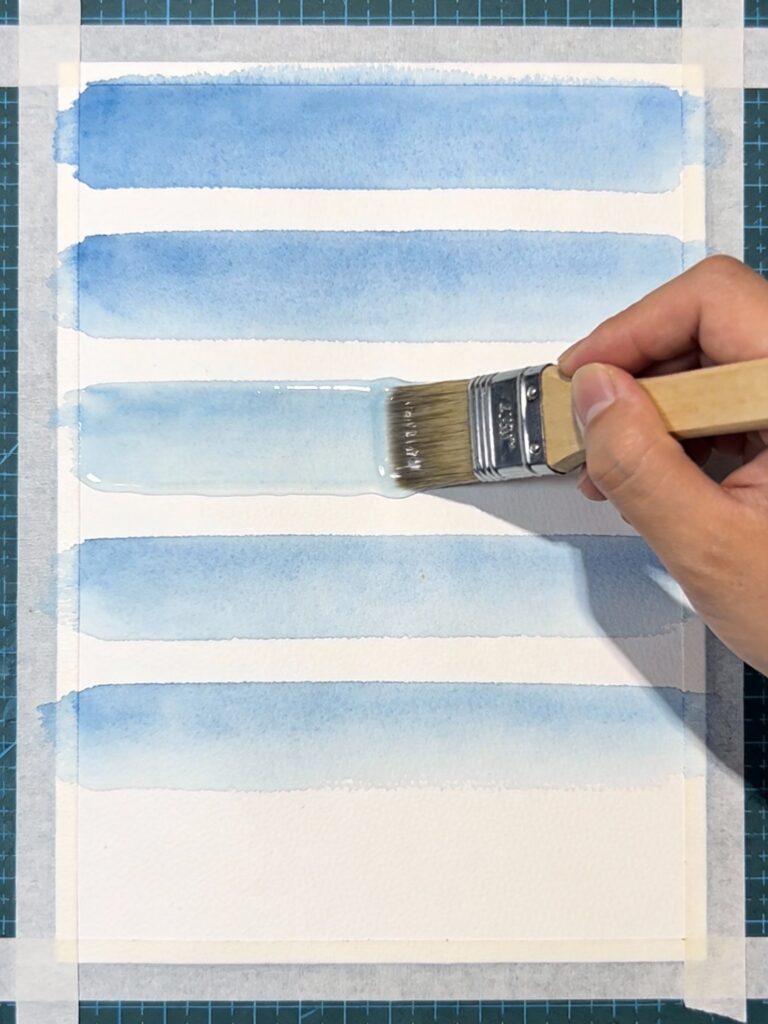 Wetting watercolor paper evenly with large flat brush in horizontal strokes for wet-on-wet technique