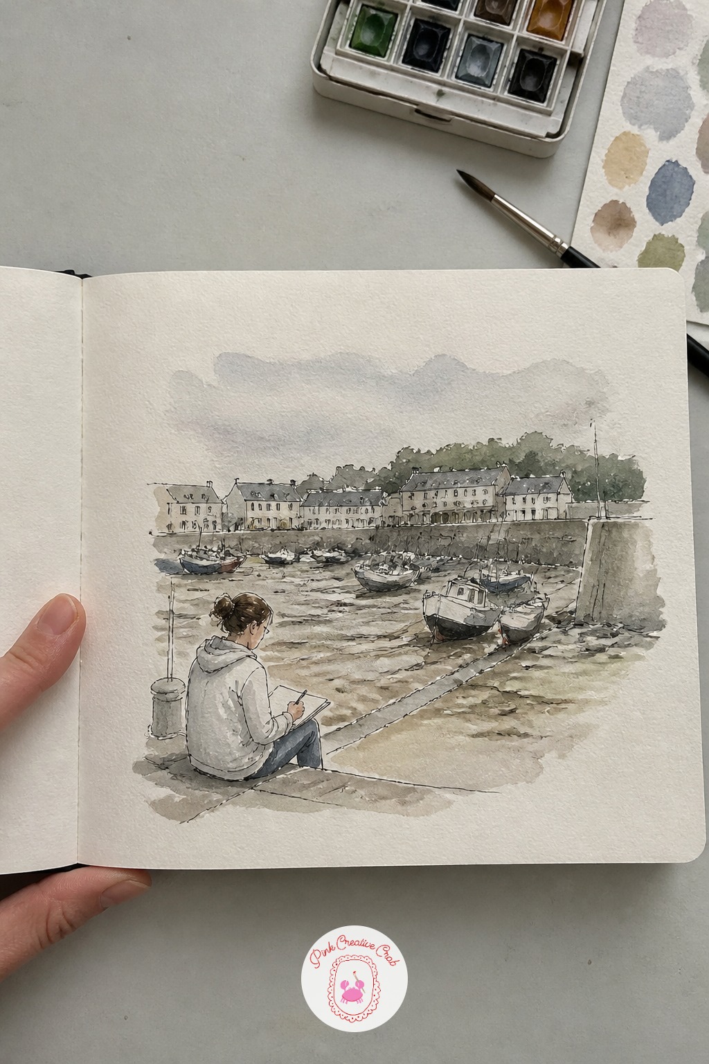 Tourist Sketching the Harbor at Low Tide — A nice quiet bridge into the more layered scenes ahead: a tourist with her own sketchbook open on her knees, boats